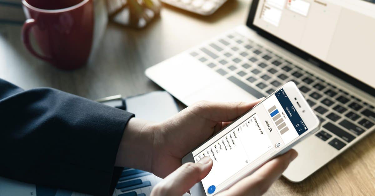 A businessman uses Smartsheet card view on a mobile device and laptop